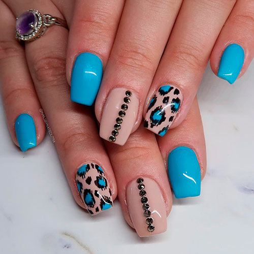 Cute blue leopard print nails on nude nails with some gold crystals on the middle nude fingernail and three light blue nails