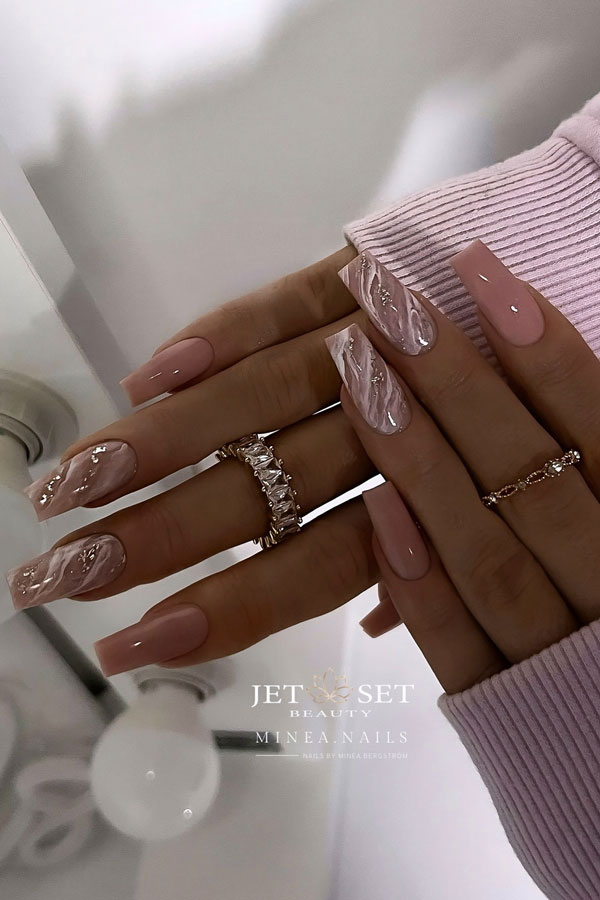 Glossy nude coffin nails with two accents adorned with white marble nail designs and a touch of gold foil