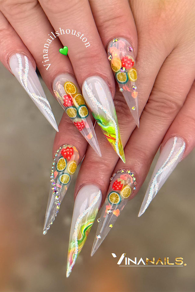 Long stiletto shaped milky white nails with fruit and rhinestones on two accent clear nails