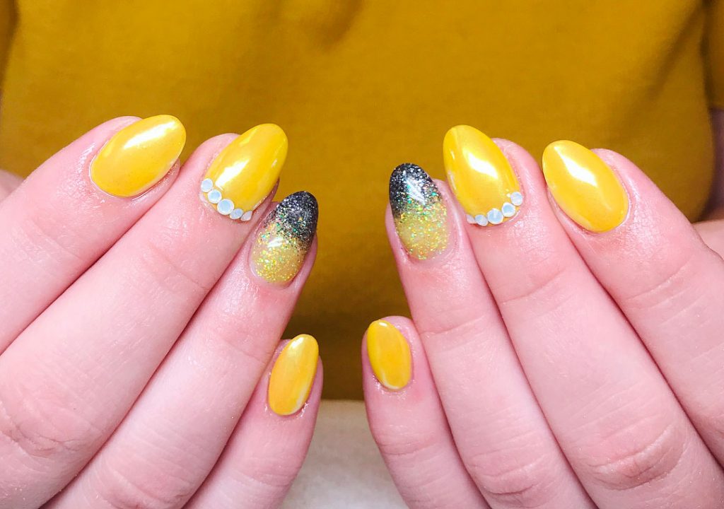 Amazing almond short yellow acrylic nails with five crystals in one nail and accent glitter nail with black tip!