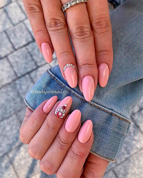Beautiful glossy light pink nails almond shaped with some crystals at the base of the ring fingernail.