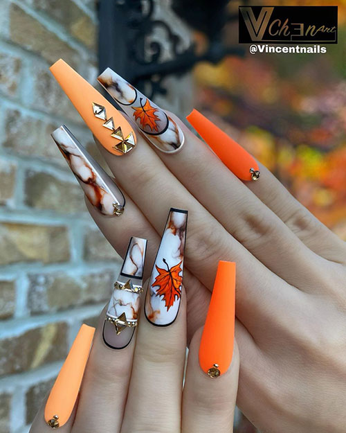 Fall nails consists of Neon orange, light orange, and marble coffin nails with leafy accent nail design