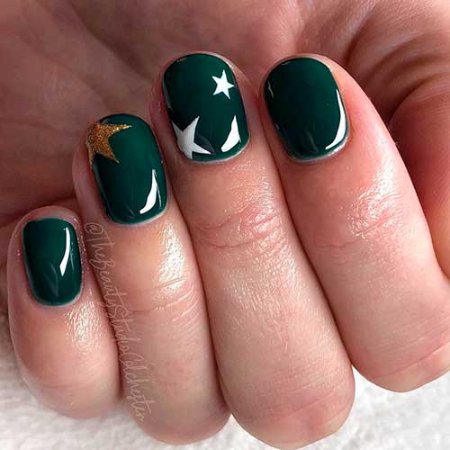 Glossy short dark green acrylic nails 2020 with painted white and gold glitter stars