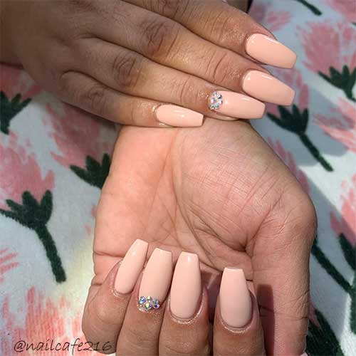 Nude coffin nails with some rhinestones on ring fingernail near the cuticle area