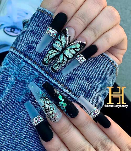 Cute coffin shaped matte black nails with rhinestones, glitter, accent floral clear nail, and two accent butterfly nails design!