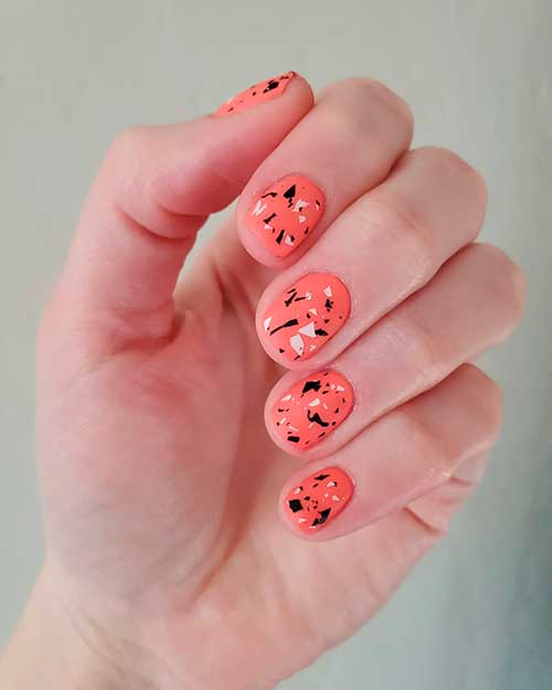 Short matte coral orange nails that uses "Love yourself to peaces" Essie nail polish with black and white shredded pieces
