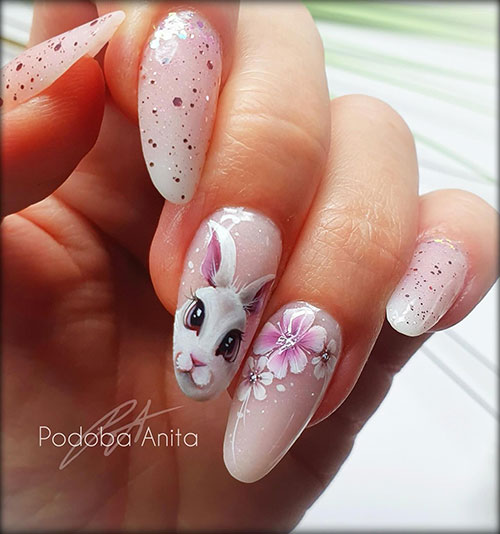 Gel French ombre Easter nails adorned with glitter as speckles and accent nails adorned with a bunny face and floral nail art