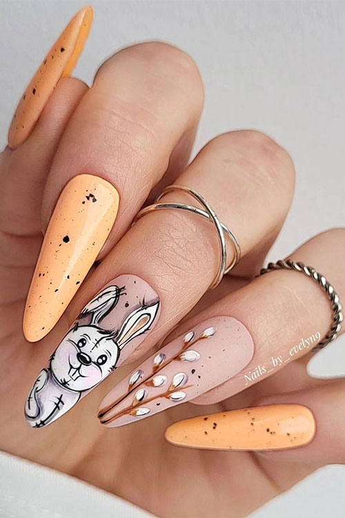 Long almond-shaped Easter peach nails with black speckles with a bunny shape and blooms on two nude accent nails