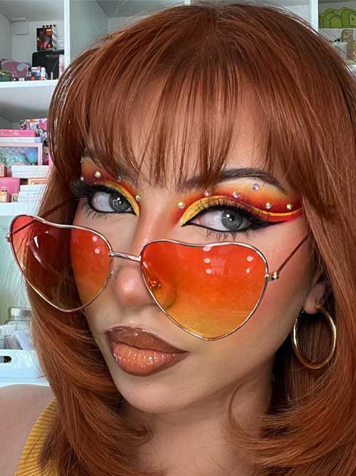 Summer makeup look featuring vibrant orange and yellow eyeshadow, rhinestones, sleek eyeliner, and deep nude lips for balance. Summer makeup look featuring vibrant orange and yellow eyeshadow, rhinestones, sleek eyeliner, and deep nude lips for balance.