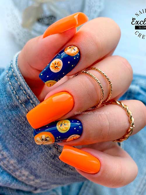 Long square shaped orange nails with orange slices on two navy blue accents for summer 2022