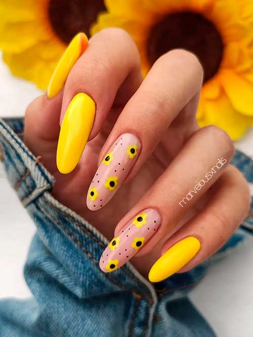 Long round shaped glossy yellow nails with tiny sunflowers and black speckles on two nude color accent nails