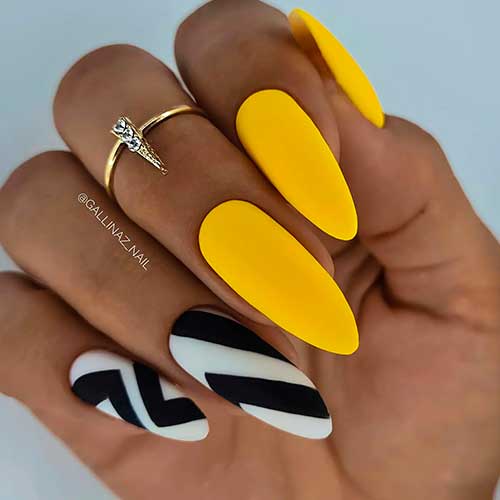 Long almond shaped matte yellow nails with two striped black and white accent nails