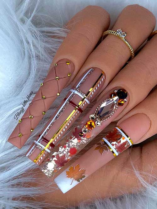 Long Nude fall nails with maple leaves, glitter, and rhinestones