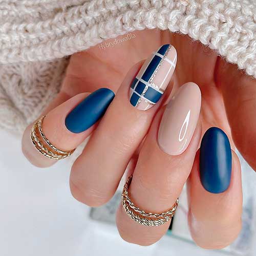 Medium round shaped navy blue and nude winter nails 2023 with plaid nail art on an accent nail