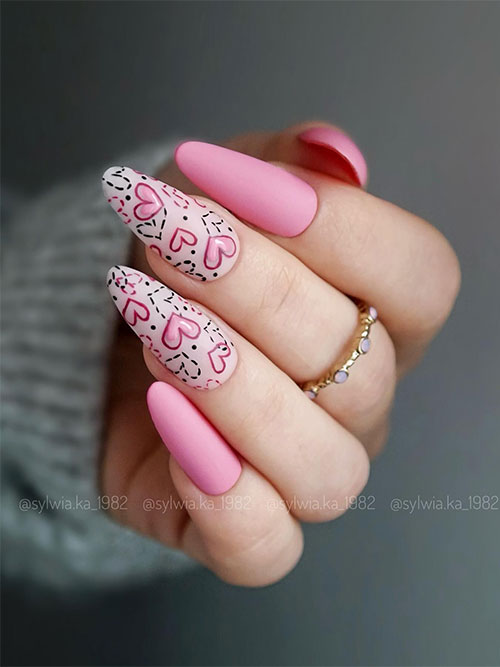 Long almond-shaped matte pink valentines nails with two light nude pink accent nails adorned with pink and black hearts