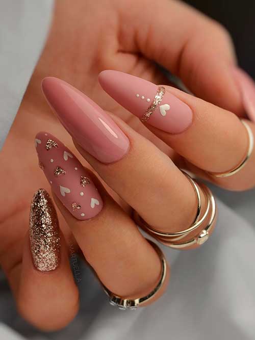 Long almond-shaped nude nails with gold glitter and tiny white hearts for valentine’s day celebration