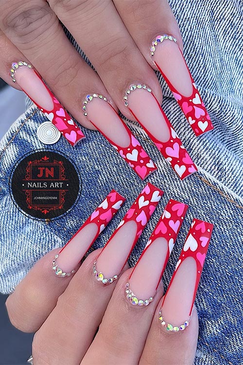 Long coffin-shaped matte red French nails with white, pink, and lilac tiny hearts adorned with rhinestones Long coffin-shaped matte red French nails with white, pink, and lilac tiny hearts adorned with rhinestones