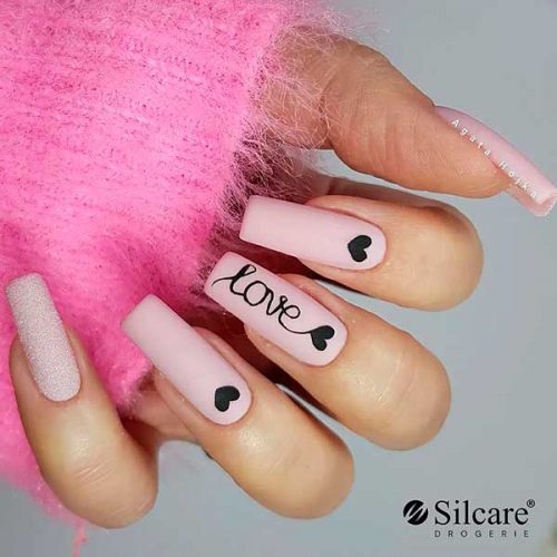 Long square shaped pastel matte pink valentine nails with black heart shapes and an accent sugar glitter nail