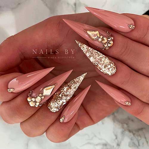 Long stiletto nude nails with gold glitter and rhinestones