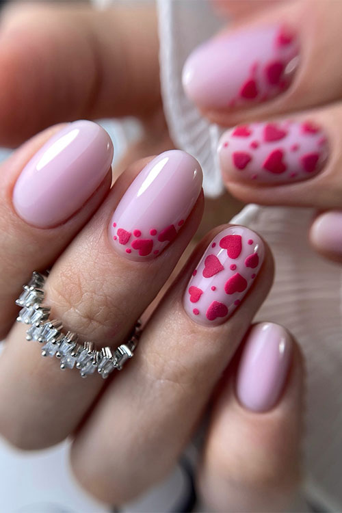 Short glossy nude pink nails with two accent nails adorned with red hearts and dots Short glossy nude pink nails with two accent nails adorned with red hearts and dots