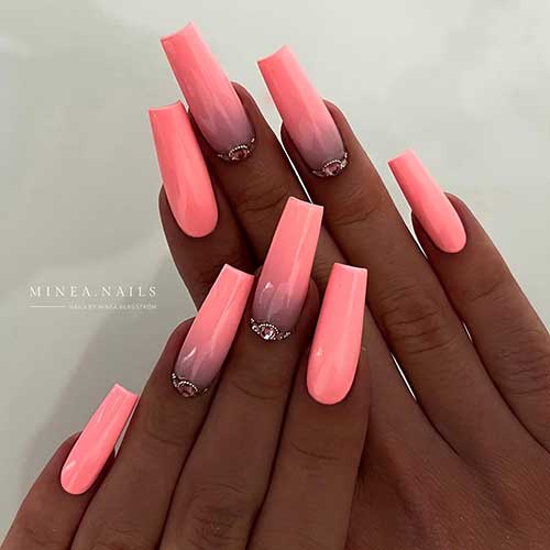 Long coffin coral bright summer nails with two ombre accent nails adorned with rhinestones