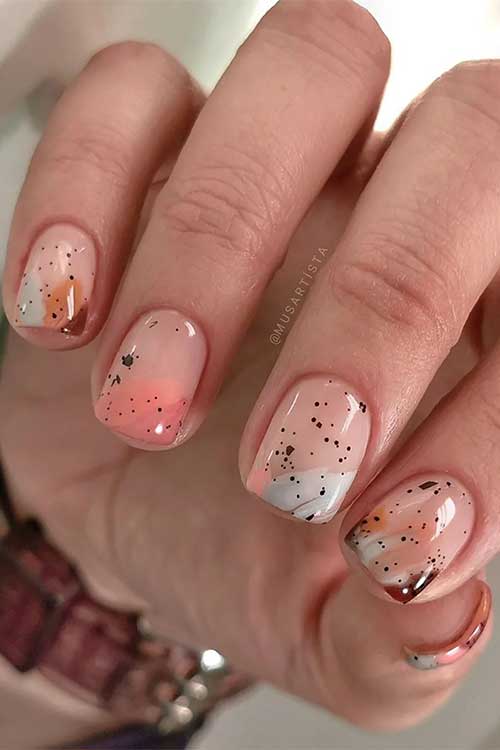 Different warm toned abstract nail art with black speckles over short nude nail tips