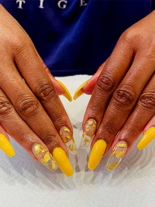 Long coffin yellow acrylic nails with gold foil patches over two clear acrylic accent nails