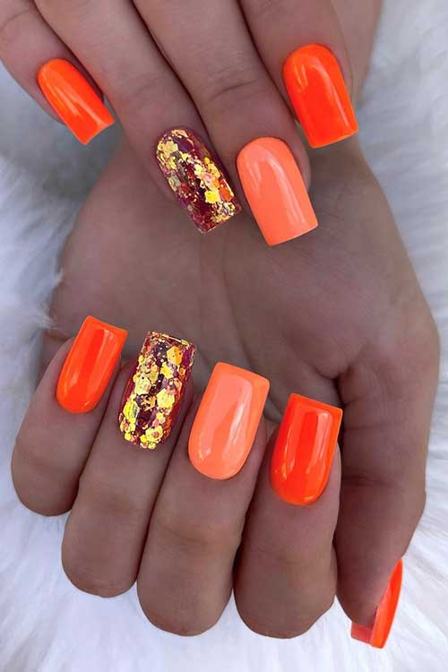 Medium square-shaped neon orange nails with gold flakes on an accent nail
