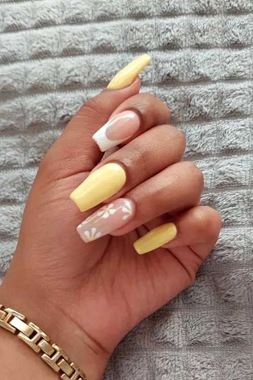 Pastel yellow acrylic nails with a white French tip and daisy flowers on an accent nail