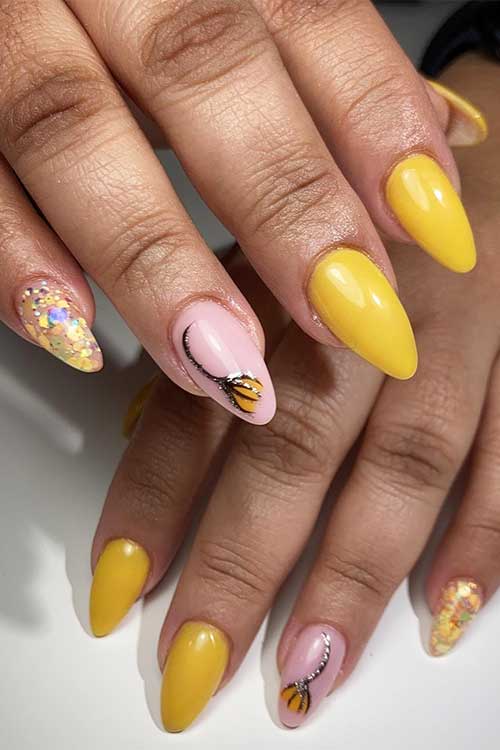 Yellow acrylic nails with a pink accent nail adorned with a flower and a glitter accent