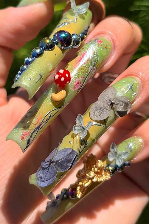 Long pastel green fairy nails with glitter and 3d items such as flowers, butterflies, and mushrooms
