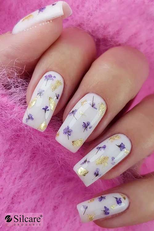 Long square shaped milky white nails with purple dried flowers and gold glitter patches 