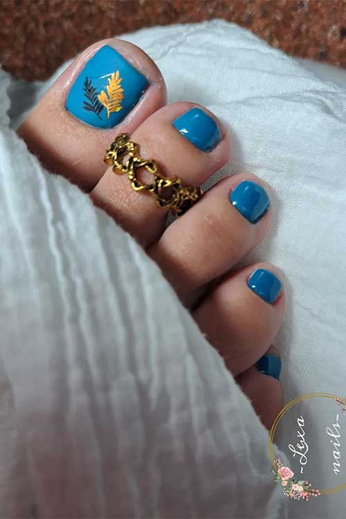 Denim blue toe nails with black and burnt yellow leaves on the big toe nail is one of the perfect fall toe nail designs