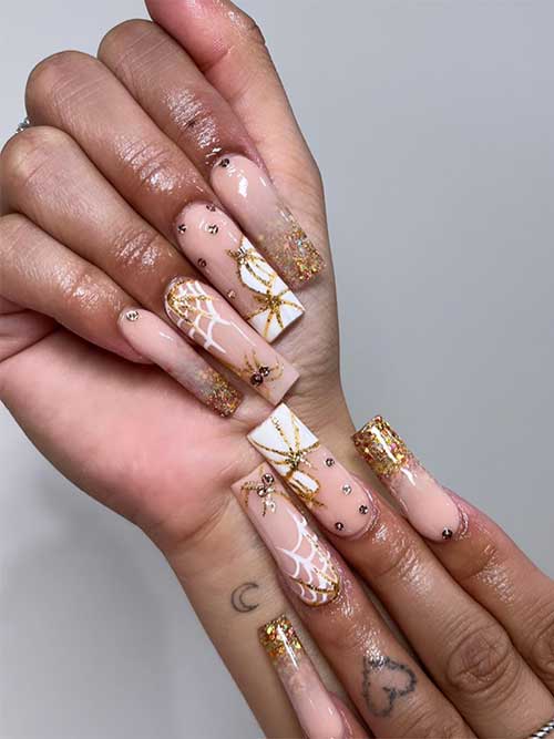 Halloween nude nails with gold glitter tips and white pumpkins and spider webs adorned with rhinestones.
