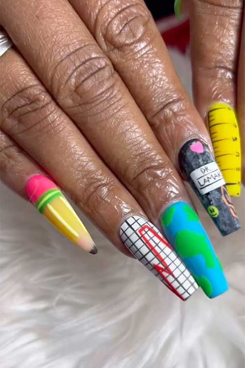 Long coffin matte nails feature a ruler, world map, crayon, notepaper, a stiletto pencil nail, and colorful rhinestones