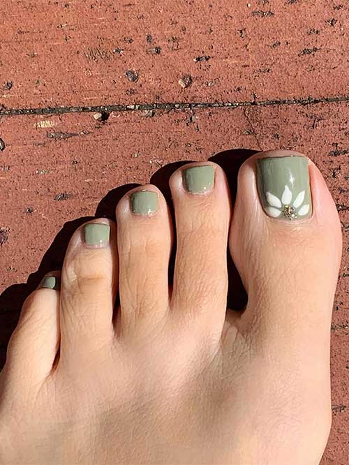 Sage green fall toe nails with a white daisy flower on the big toe adorned with some glitter on the flower’s center.