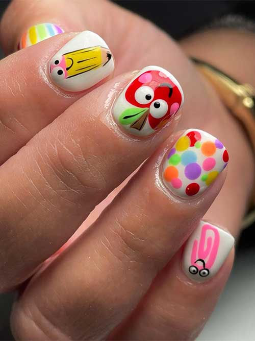 Short back to school nails with white base color and features apple, pencil, paper clip, colorful polka dots, and ABCs