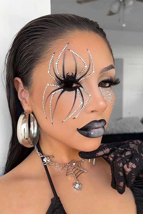 Creative spider makeup with black lips, a big black and silver rhinestone spider on one eye, and a rhinestone cobweb