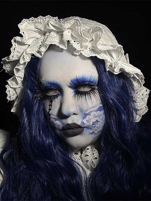 Creepy doll makeup with blue eyeshadow, long lashes, dark brown lips, and scary eye contacts