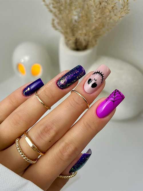 Dark purple Halloween nails with glitter and nude and magenta accent nails feature a cobweb and a scary face