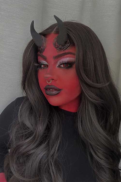 Devil makeup with black horns, red face and hands, black lips, and red eye contacts