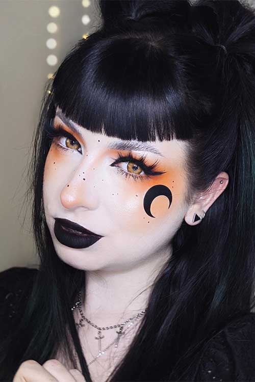 Goth girl Halloween makeup looks scary 2023 with orange eyeshadow, celestial art, black lips, and scary yellow eye contacts