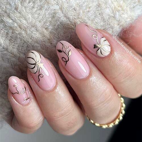 Medium almond shaped white pumpkin nails adorned with gold outer lines and gold leaves.