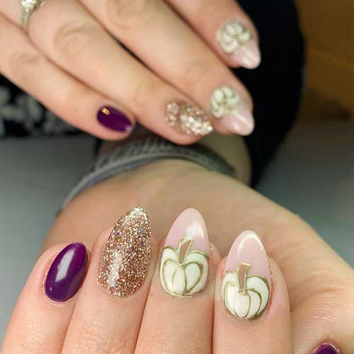 Purple and gold glitter manicure with two accent nude nails with white pumpkin nail art adorned with gold outlines.
