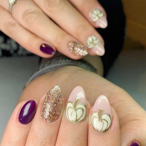 Purple and gold glitter manicure with two accent nude nails with white pumpkin nail art adorned with gold outlines. Purple and gold glitter manicure with two accent nude nails with white pumpkin nail art adorned with gold outlines.