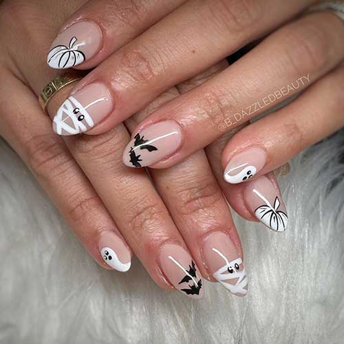 Short white and black Halloween nails over nude base color and feature pumpkin nail art, bats, mummies, and ghosts.