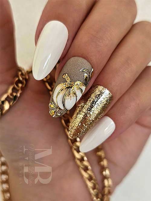 White almond nails with gold glitter accent nail and white and gold pumpkin nail art on another accent nail. White almond nails with gold glitter accent nail and white and gold pumpkin nail art on another accent nail.