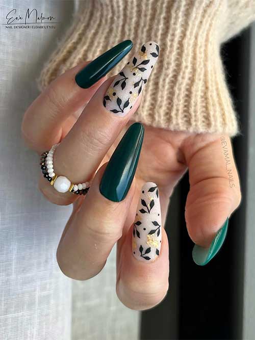 Long dark green nails with two accent milky white nails adorned with black leaves and gold foil flakes