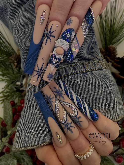 Long festive matte nude and blue Christmas nails with rhinestones, blue snowflakes, and a Santa Claus on an accent nail