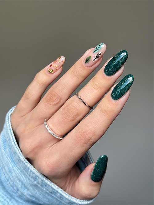 Long glitter dark green nails with two accent nude nails adorned with leaf nail art and gold and bronze foil flakes